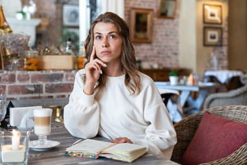 Cute white girl thinking while having breakfast in cafe. beautiful young European sits in cafe and dreams