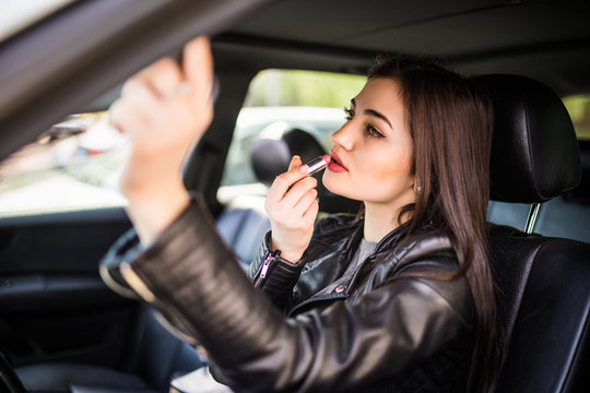 Young attractive woman looking in rear view mirror painting her lips doing applying make up while driving the car.