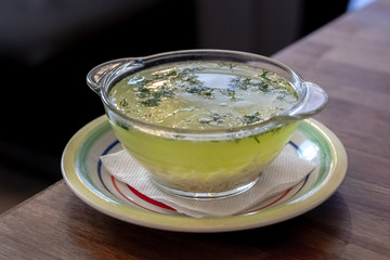 hot chicken soup at glass plate with eggs,meal,parsley and noodles.wooden table background. healthy lifestyle concept.