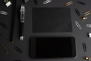 Flat lay, black style.Set of stationery accessories mock up on black background, phone, black card.