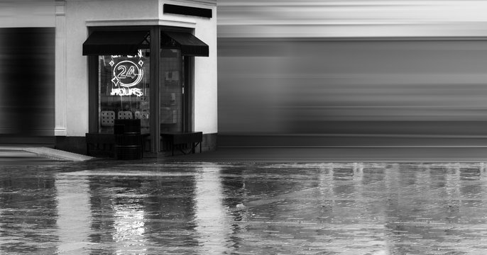 Open 24 Hours neon sign on a restaurant window with italian awnings. Summer rainy day