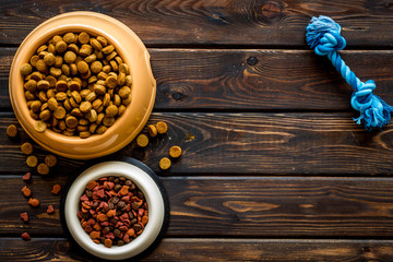 Dry pet food in bowls and toys on wooden background top view space for text