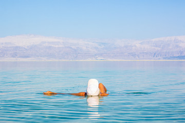 floating woman on calm peaceful Dead sea water surface in health care Israeli resort territory,...