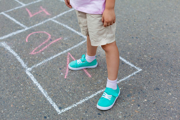 Close-up of Childs legs and classics painted on asphalt. little girl playing hopscotch game on playground outside on a sunny day. Summer activities for children