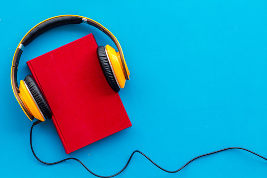 Books with headphones for listening to audiobook on blue background top view copy space
