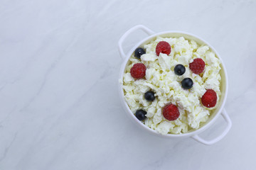 Bowl with cottage cheese and fresh berries on light background