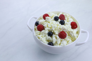 Bowl with cottage cheese and fresh berries on light background