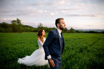 Wedding. Bride and groom holding hands and walk on the green field