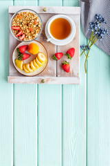 Breakfast on the tray with granola, tea and fruit on mint green wooden background top view mockup