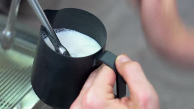 Whipping white milk in an blac coffee pot using a special tube of the coffee machine
