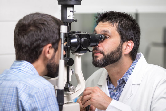 Male Doctor Ophthalmologist Is Checking The Eye Vision Of Handsome Young Man In Modern Clinic. Doctor And Patient In Ophthalmology Clinic .