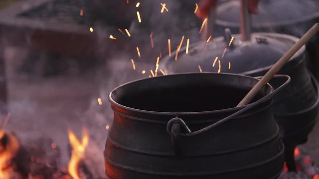 Placing hot coals underneath cauldron from campfire to cook potjiekos, a South African traditional dish.
