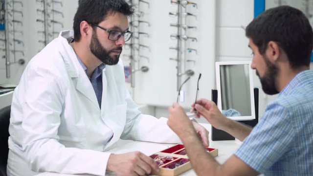 doctor ophthalmologist is helping a client to choose the most appropriate glasses in ophthalmologic clinic .