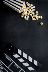 Movie premiere concept with clapperboard, popcorn on black background top view space for text