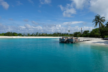 Outdoors sunbathing terrace platform in Maldive island resort above blue green sea water, with wide sunny blue sky white cloud and green palm trees