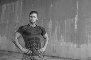Black and white. Muscular model in fashion sportswear on urban gray background. Portrait of brutal strong guy with a modern trendy hairstyle. Sports young man working out outdoor.
