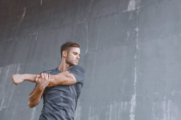 Athlete doing stretching warmup exercise. Male fitness model in fashion sportswear in city. Runner sprinting on urban gray background.