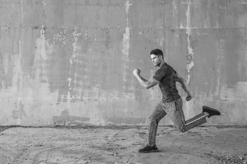 Black and white. Athlete doing sprint hiit high intensity interval training. Male fitness model in fashion sportswear in city. Runner sprinting on urban gray background.