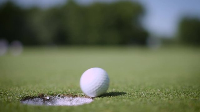 Close up golf ball falling in hole on putting green, 4K slow motion