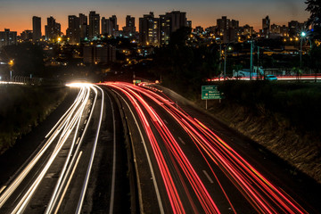 Obraz premium Marilia, Sao Paulo, Brazil, June 12, 2019. Trail of light caused by vehicular traffic in SP-294, Comandante Joao Ribeiro Barros Highway with buildings from downtown in the background, in Marília,