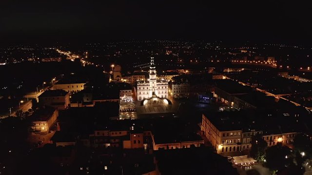 Zamosc, Lublin voivodeship. The city in Poland at night. The drone view. The drone is moving backwards focusing on the city hall in slow motion. The beauty of the illuminated city.