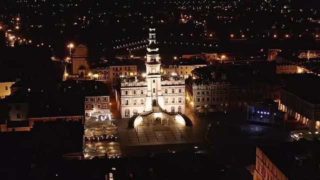 Zamosc, Lublin voivodeship. The city in Poland at night. The drone view. The drone is moving backwards focusing on the city hall in slow motion. The beauty of the illuminated city.