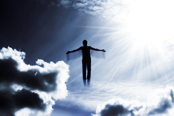 Silhouette of a man flying up in the sky in the bright rays of the sun with arms spread apart.