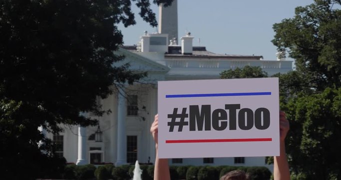 A man holds a #MeToo protest sign outside the White House.  	