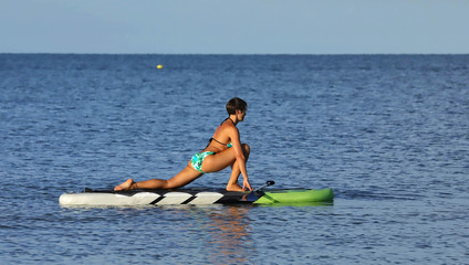 Beautiful woman challenges herself by practicing yoga on a paddle board .