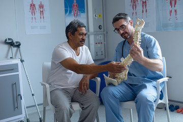 Male orthopedic surgeon explaining spine model to male patient