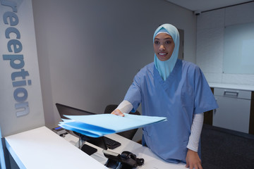 Female surgeon in hijab standing with medical report file at reception in hospital