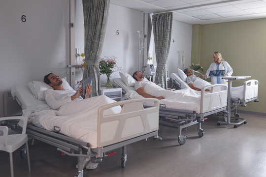 Male patient using digital tablet while female doctor checking male patient in the ward