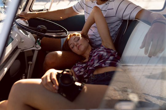 Beautiful woman relaxing on man lap in front seat of camper van at beach