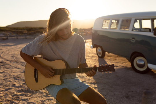 Young man playing guitar near camper van at beach