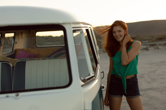 Beautiful happy woman standing near camper van at beach