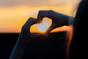 Silhouette of a young girl holding sun in her hands shaped like heart at sunset