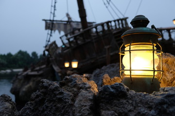 close up warm yellow light of retro beacon light on grey stones. Blurred dark pirate ship wreckage...