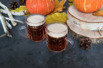 Two mugs of cold dark beer with pumpkins and autumn leaves on a wooden background. Halloween season. Beer day. Oktoberfest.