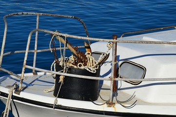 Bucket with anchors, rusty chain and ropes tied to steel railing on front of roofed white fishing boat