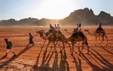 Fototapete Marokko Frauen reiten durch die Wüste im Wadi Rum, Jordanien, auf Kamelen, die von Beduinenführern geführt werden.