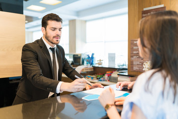 Manager Pointing On Form To Man And Woman In Hotel