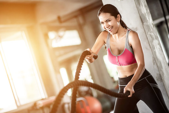 Young healthy woman exercising with battle rope at the gym