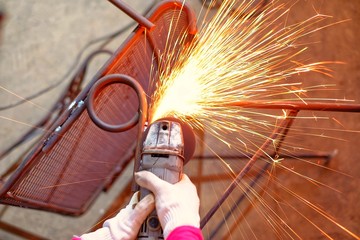 A Indian woman wearing a pink long sleeve jacket and protective gloves is welding and grinding a...