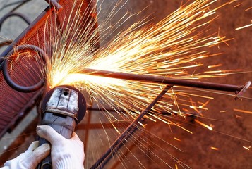A Indian woman wearing a pink long sleeve jacket and protective gloves is welding and grinding a...
