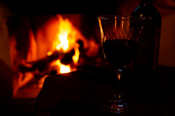 Bottle and glass with wine in the foreground and the background fireplace with high flames.