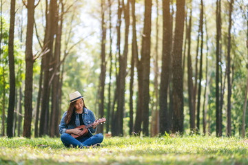 Fototapeta premium A beautiful asian woman sitting and playing ukulele in the outdoors