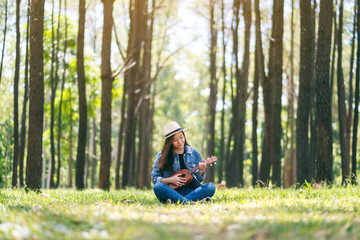Naklejka na ściany i meble A beautiful asian woman sitting and playing ukulele in the outdoors