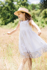 Little girl in a hat runs on a golden meadow