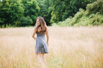 Naklejka na ściany i meble Girl in a dress in the field, view from the back