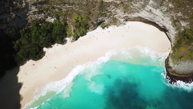 Bird's Eye Drone shot above waves crashing onto KelingKing beach on the island of Nusa Penida, Indonesia. The water is a beautiful shade of blue.